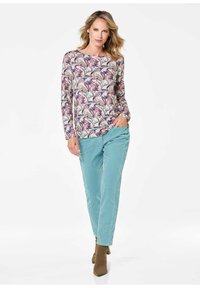 Leichtes, langärmliges Oberteil mit einem wirbelnden Muster in Pink, Lila und Blau; kombiniert mit mintgrünen Hosen und braunen Stiefeletten.