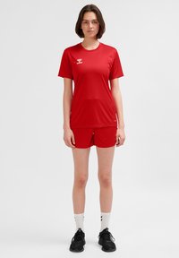 Rotes sportliches T-Shirt mit Rundhalsausschnitt und kurzen Ärmeln, dazu passende rote Shorts. Beide sind aus leichtem, glattem Stoff gefertigt.