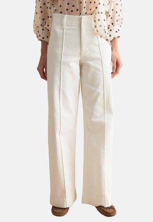 Pantalon blanc taille haute à jambe large avec coutures avant, porté avec un chemisier beige à pois et des mocassins marron.