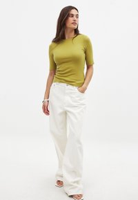 Vihreä limen värinen istuva toppi, jossa on lyhyet hihat, yhdistettynä väljään valkoiseen korkeavyötäröiseen housuun. Malli seisoo yksinkertaisella taustalla.