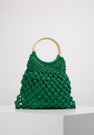 Zielona torebka makramowa z drewnianymi okrągłymi uchwytami, prezentowana na białym piedestale na jednolitym tle.