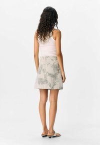 Jupe légère beige à motif floral avec des plis, dotée d'une taille ajustée et d'une coupe légèrement évasée, associée à des sandales noires simples.