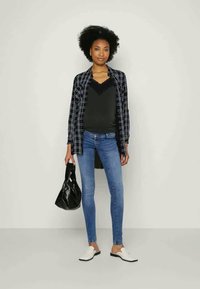 Musta-valkoinen ruudullinen takki, musta pitsireunuksinen paita, siniset kapeat farkut ja valkoiset liukupohjakengät. Pitää kädessään mustaa käsilaukkua.