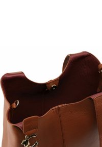 Borsa a tracolla in pelle marrone con fodera interna color bordeaux, ferrature dorate e apertura superiore con linguetta di chiusura a scatto.