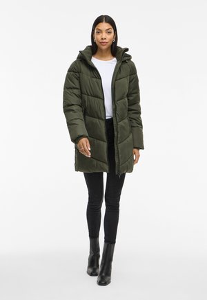 Olivově zelená péřová bunda s kapucí, se zapínáním na zip a prošívaným designem. V kombinaci s černými skinny jeans a kotníkovými botami.