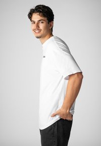 Weißes Baumwoll-T-Shirt mit rundem Ausschnitt und kurzen Ärmeln, mit schwarzem Aufdruck. Wird mit dunkler Jeans getragen und präsentiert eine lässige Passform.