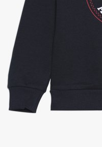 Felpa blu navy con polsini e orlo a coste, caratterizzata da una texture liscia e un dettaglio grafico rotondo sul davanti in colori a contrasto.