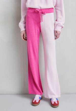 Pantalons décontractés rose et rose clair avec une taille à lien. Texture douce et design évasé. Portés avec des baskets colorées.