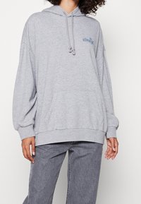 Sudadera de algodón gris con un ajuste holgado, bolsillo canguro, capucha con cordones y detalle del logo azul en el pecho. Cuenta con mangas largas con puños.