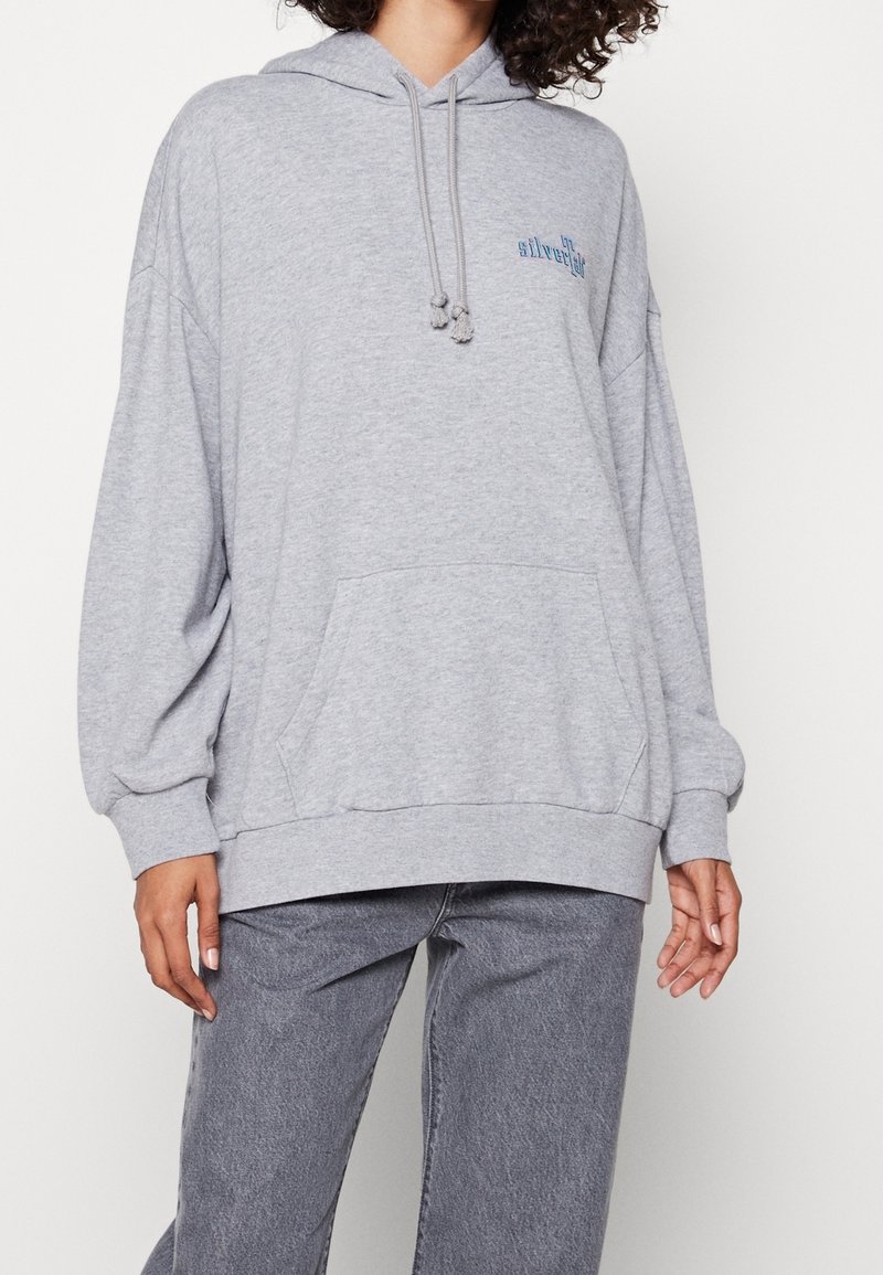 Sudadera de algodón gris con un ajuste holgado, bolsillo canguro, capucha con cordones y detalle del logo azul en el pecho. Cuenta con mangas largas con puños.