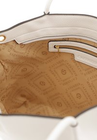 Interieur van een wit leren handtas met geëmbosserd logo, gouden rits en een gladde stoffen voering met een subtiel beige patroon.