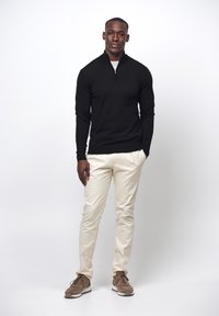 Schwarze Zip-up- sweatshirt, beiger Hosen und braune Sneakers. Glatter Stoff, figurbetontes Design und neutrale Farben schaffen einen lässigen Look.