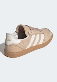 Beige mockasinsneaker med vit tre-randig design, gummisula och vadderad krage. Perforerade detaljer på hälen.