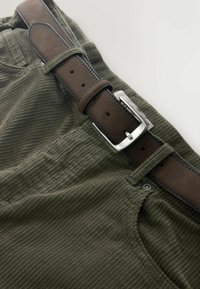 Olivgrüne Cordhose mit braunem Ledergürtel, der eine silberne Metallschnalle und sichtbare Nähte entlang der Kanten aufweist.