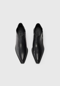 Botas de cuero negro hasta el tobillo con un diseño de puntera puntiaguda y estilo sin cordones. Textura suave y acentos mínimos visibles.