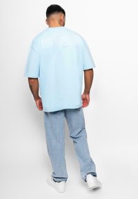 Lyseblå oversized t-shirt med ordet "DROPSIZE" trykt på ryggen. Bæres med lyseblå jeans og hvide sneakers. Casual pasform.