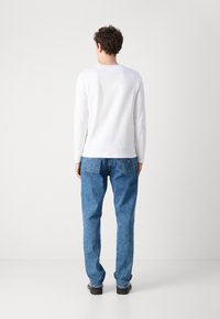 Hvit skjorte med lange ermer, kombinert med blå denimjeans med rett ben-design og synlige baklommer. Enfarget, avslappet stil.