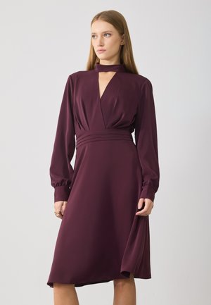Burgundy dress with long sleeves, deep V-neck, and a fitted waist. Features a front cut-out and flowing A-line skirt. Smooth, lightweight fabric.