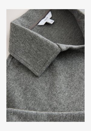 Camisa gris con cuello, confeccionada en un tejido de punto texturizado, que presenta un cuello doblado y detalles visibles de costuras a lo largo de los bordes.