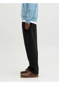 Pantalones de chándal negros con un corte relajado, combinados con una sudadera ligera azul y zapatos de barco marrones. Presenta una textura suave y un diseño sencillo.