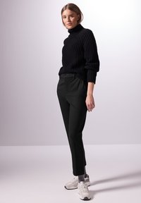 Pull à col roulé noir côtelé associé à un pantalon noir ajusté et des baskets gris clair. La tenue présente une coupe décontractée et une texture douce.