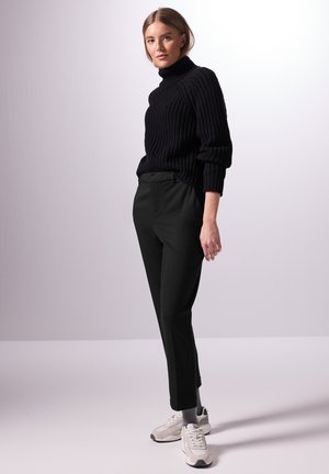 Pull à col roulé noir côtelé associé à un pantalon noir ajusté et des baskets gris clair. La tenue présente une coupe décontractée et une texture douce.