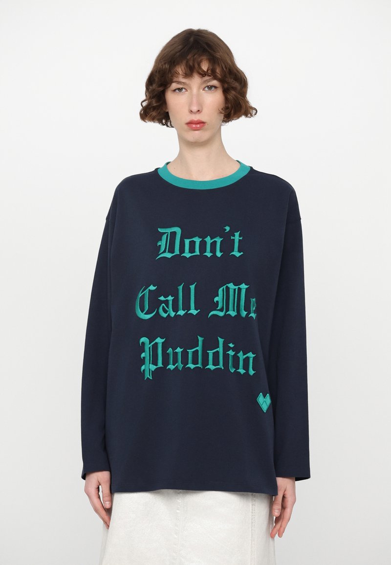 Marineblå langermet sweatshirt med turkise detaljer i kragen og tekst med stor skrift: "Ikke kall meg Puddin." Har hjertetilbehør i nederkant.