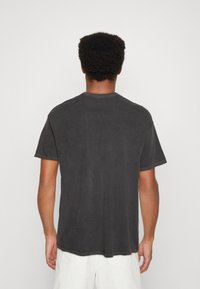 Tmavě šedé bavlněné tričko s krátkými rukávy, kulatým výstřihem a minimálními švy. Tkanina vypadá měkce s jemnou strukturou.