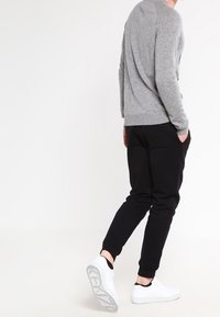Grijze gebreide trui met een ronde hals, gecombineerd met zwarte joggerbroeken en witte sneakers. De stof is soepel en de pasvorm is ontspannen.
