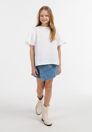 Hvid tekstureret top med flagrende ærmer, blå denimnederdel med flosset kant og cremefarvede ankelstøvler med dekorativ syning.