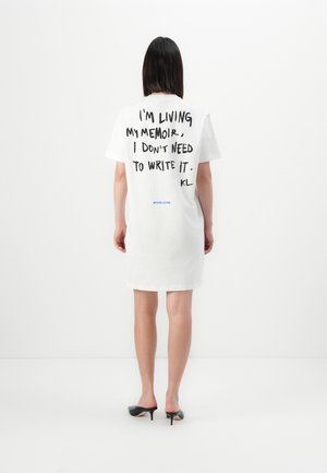 Vit bomullst-shirtklänning med korta ärmar. På baksidan i fet svart text står det: "JAG LEVER MIN MEMOAR, JAG BEHÖVER INTE SKRIVA DEN."