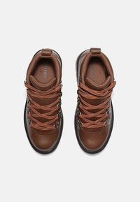 Scarpe da trekking in pelle marrone con lacci arancioni, occhielli metallici, colli imbottiti e suole in gomma nera texturizzata. Progettate per l'uso all'aperto.