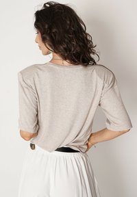 Beżowa bluzka z krótkim rękawem o luźnym kroju i okrągłym dekolcie, charakteryzująca się miękką fakturą, w połączeniu z białymi spodniami na gumce w talii.