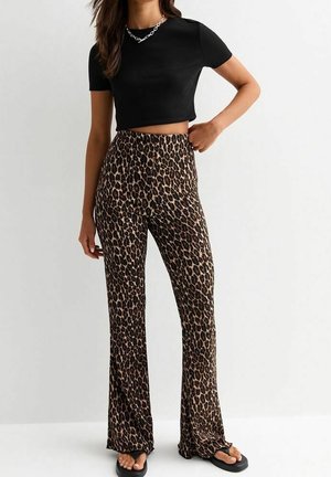 Vrouw draagt een zwart cropped t-shirt, luipaardprint hoge taille wijde broek, zwarte slippers en een zilveren ketting.