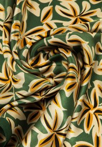 Tessuto verde con un motivo floreale astratto giallo, nero e crema, attorcigliato e piegato per mostrare la texture e il design.
