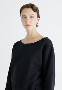 Sweatshirt preto com decote amplo, mangas longas e um tecido texturizado. Apresenta um detalhe de costura discreto na frente.