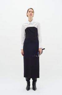 Rochie neagră cu un corset ajustat, fustă lungă și cămașă albă cu nasturi pe dedesubt. Botine negre ascuțite și o poșetă neagră ca accesorii.