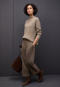 Beige gestrickter Pullover, braune karierte weite Hosen, braune Wildleder-Stiefeletten und eine passende braune Tasche. Minimalistisches Design mit strukturiertem Stoff.