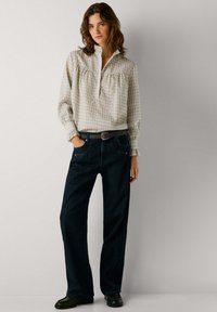 Blusa de manga larga blanca y verde a cuadros con un pequeño cuello, combinada con unos vaqueros de pierna ancha azul oscuro y un cinturón negro con hebilla metálica.