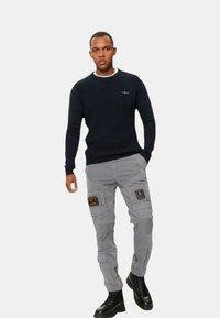 Maglione a coste blu navy con scollatura rotonda, abbinato a pantaloni cargo grigi con tasche applicate e stivali da combattimento neri.