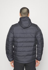 Piumino blu scuro con cappuccio, caratterizzato da un design trapuntato e una texture liscia e lucida. Le maniche a costine e l'orlo conferiscono struttura.