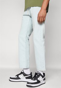 Jeans rectos de mezclilla de color azul claro, con un diseño limpio y una textura sutil, combinados con zapatillas deportivas en blanco y negro.
