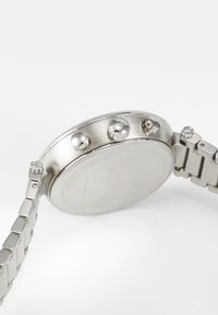 Sølv rustfritt stål klokke med rund klokkesak, tre trykkere og en metallarmbånd med børstet finish og polerte detaljer.