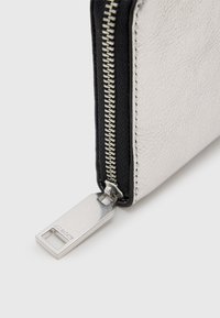 Zilveren leren portefeuille met zwarte accenten, voorzien van een zichtbare rits en metalen hardware, met een gestructureerd oppervlak.