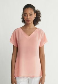 Blusa leggera color pesca con scollo a V e maniche corte a sbuffo. Tessuto morbido e trasparente con una silhouette fluida.