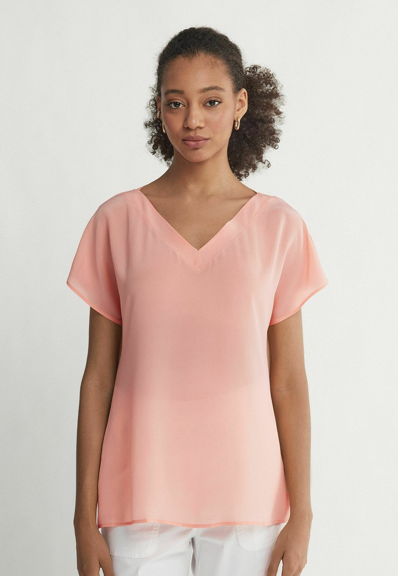 Blusa leggera color pesca con scollo a V e maniche corte a sbuffo. Tessuto morbido e trasparente con una silhouette fluida.