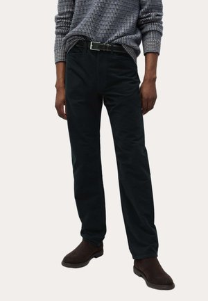 Donkergroene corduroy broek met een slanke pasvorm, voorzien van een platte voorkant, rechte pijpen en opvallende textuur. Gedragen met een gebreide trui met patroon.