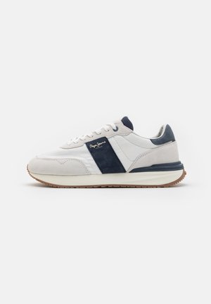 Zapatilla blanca con acentos y cordones de ante azul marino, que presenta una suela de goma texturizada y un upper de cuero suave. Logotipo en el panel lateral.