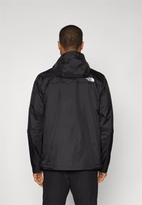 Schwarze wasserdichte Jacke mit Kapuze, ausgestattet mit einem dezenten Logo auf dem oberen Rücken und langen Ärmeln. Leicht, mit glatter Textur und lässigem Design.