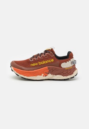 Brun og orange New Balance løbesko med tyk tekstureret sål og gult mærke på siden.